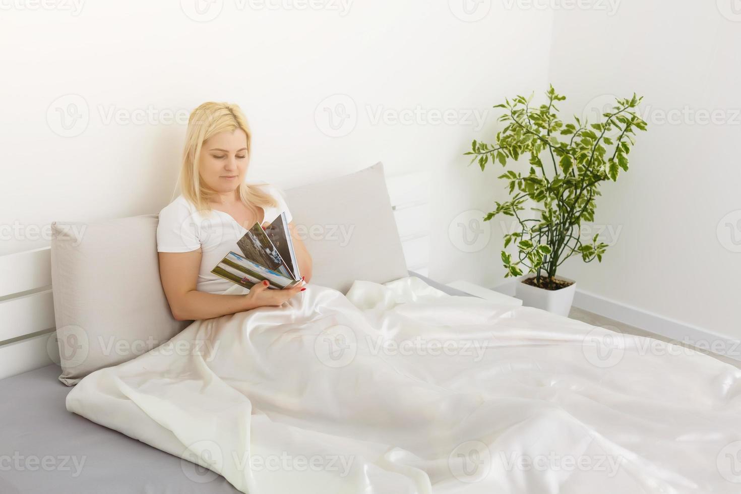 Woman holding with photo book and sitting on bed