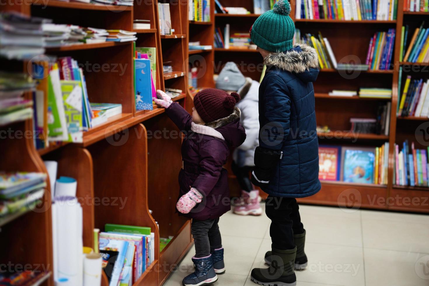 Little cute baby in jacket reaching a book from bookshelf at the library. Learning and education of european kids. photo