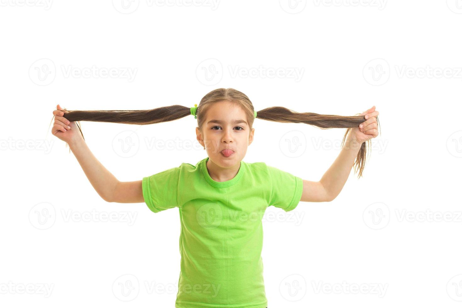 niña divertida en camisa verde sosteniendo sus colas en las manos foto