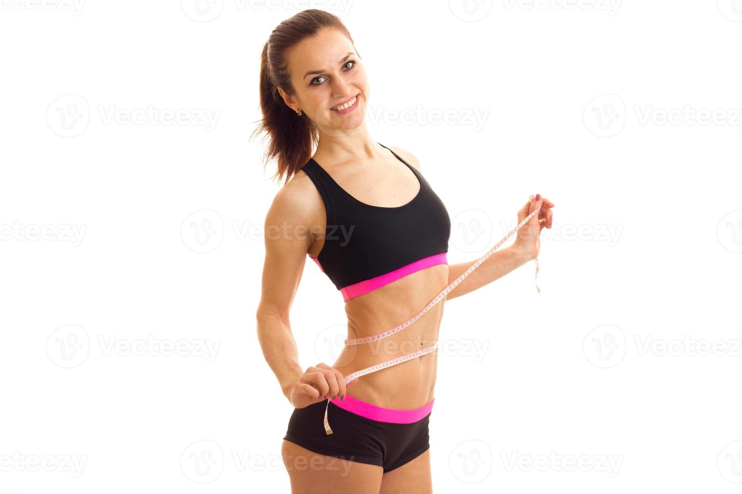 smiling sports girl in top and shorts takes the waist measuring tape photo