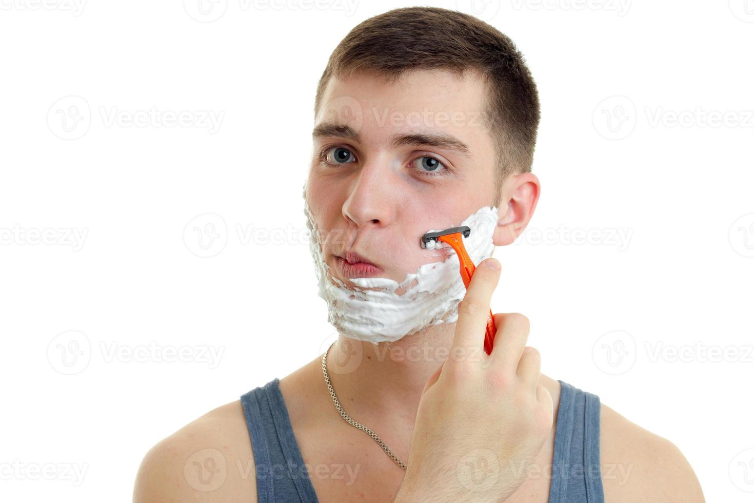 Chico joven se afeita la cara con espuma de afeitar aislado sobre fondo blanco. foto