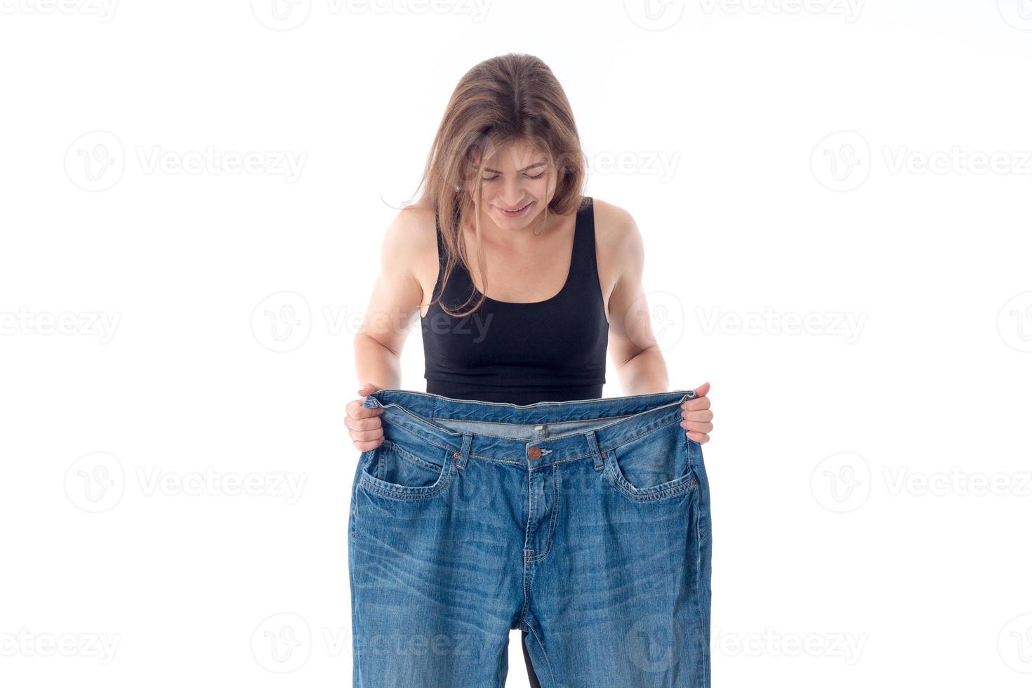 Una joven delgada mira los enormes pantalones anchos aislados de fondo blanco foto