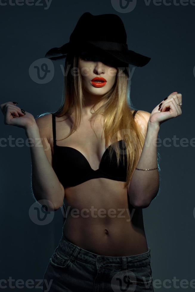 slim young girl in black bra with red lips wearing a hat with wide brim in studio photo