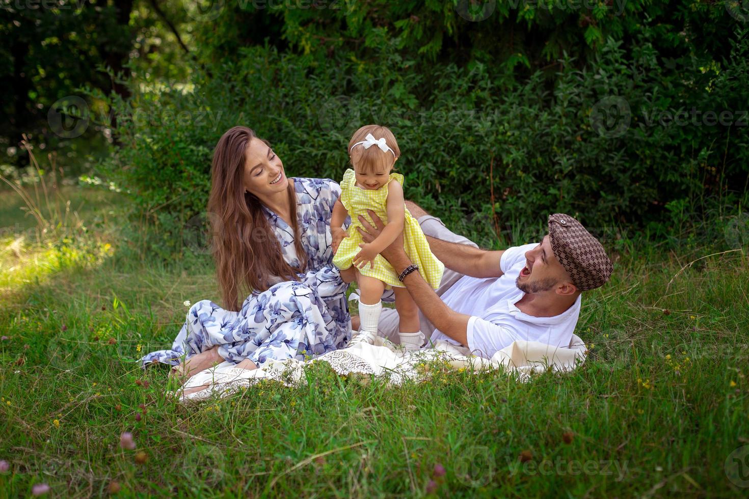 retrato de una familia joven y alegre juega con su hijita en el prado grren foto