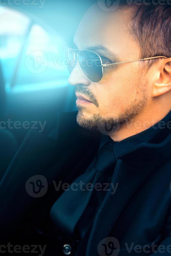 hombre adulto magnífico en traje negro y gafas de sol en coche foto