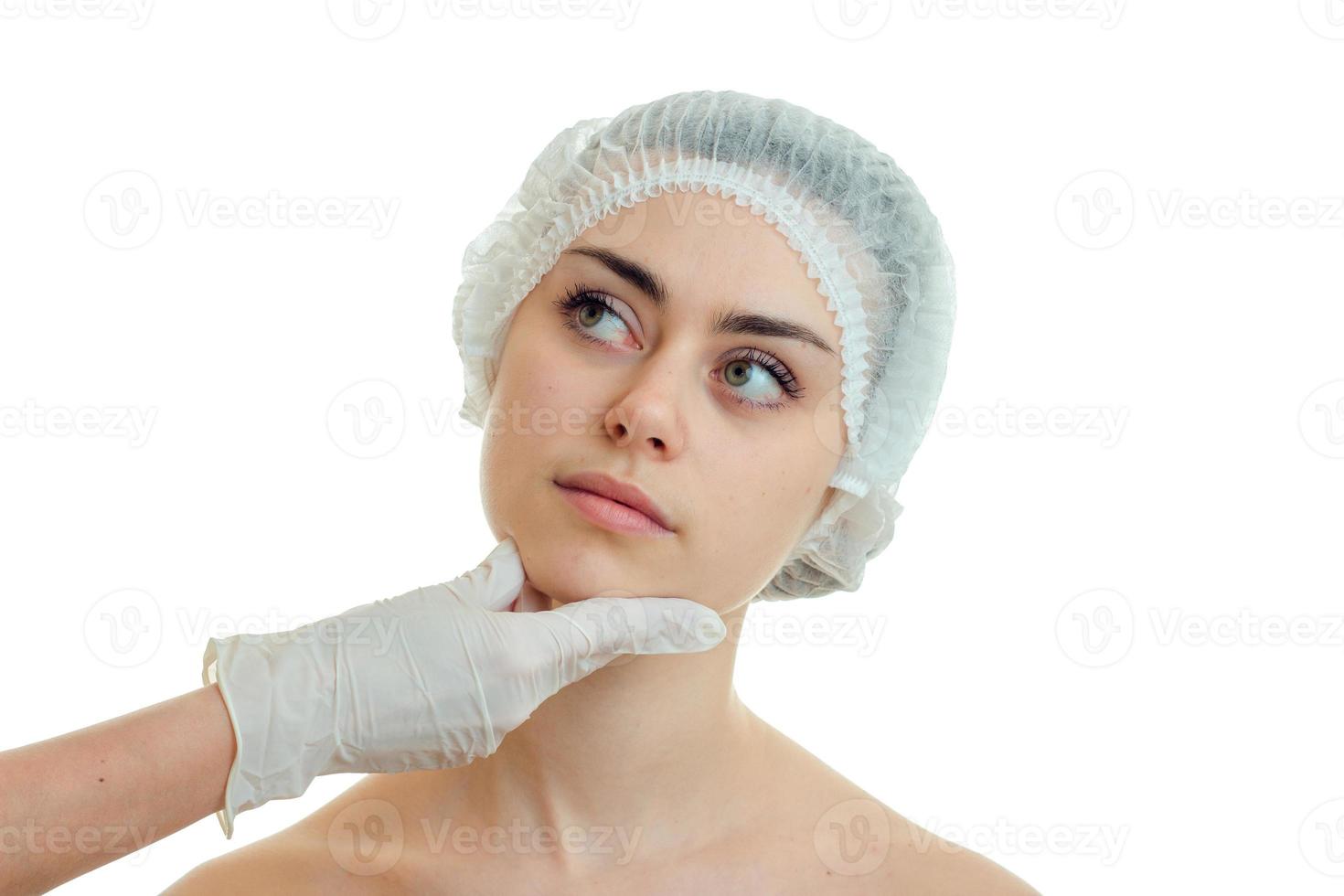 cirujano en guante revisa la cara de una hermosa chica con una gorra especial para el primer plano del cabello foto