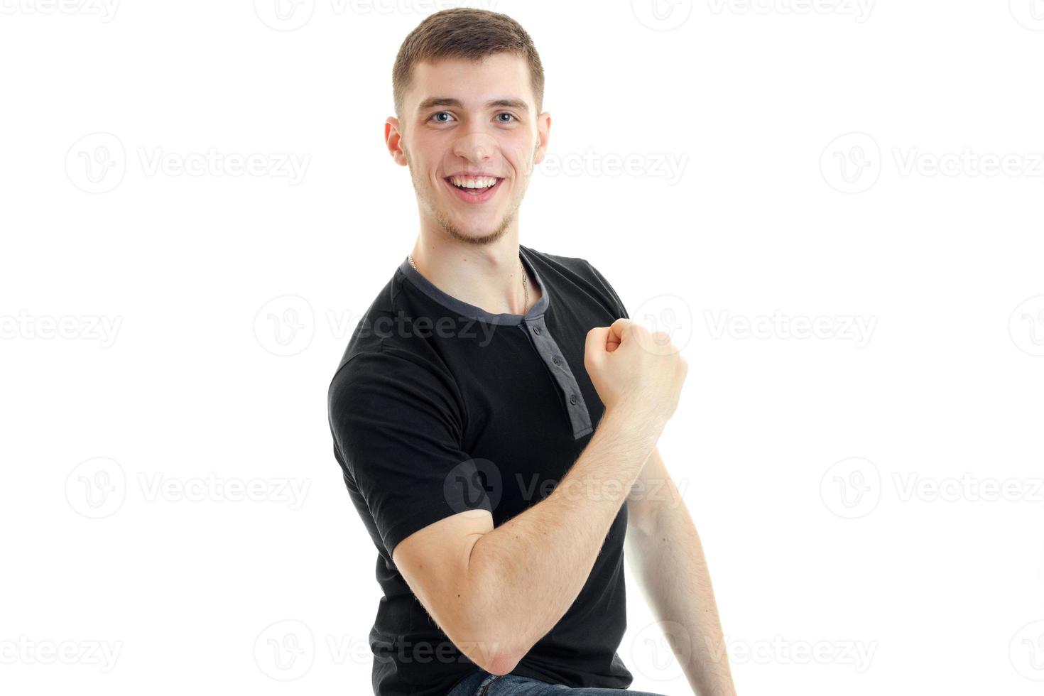 a cheerful young man in a black t-shirt shows the muscles of the arm and laughs close-up photo