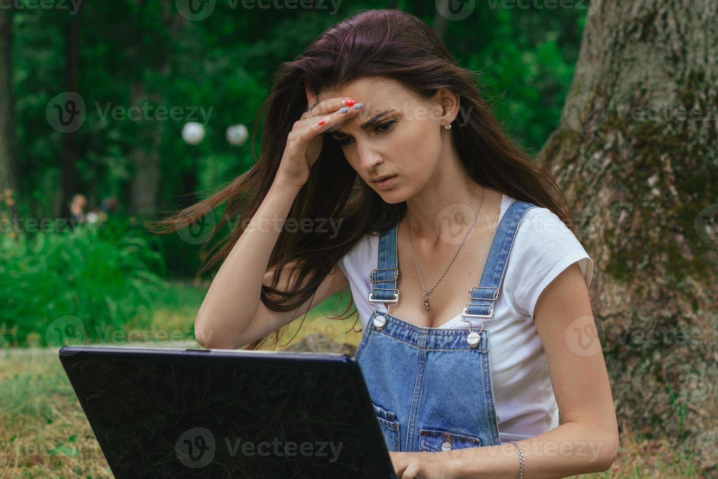 una niña mantiene la pelota detrás de la cabeza y mira la computadora portátil en el parque foto