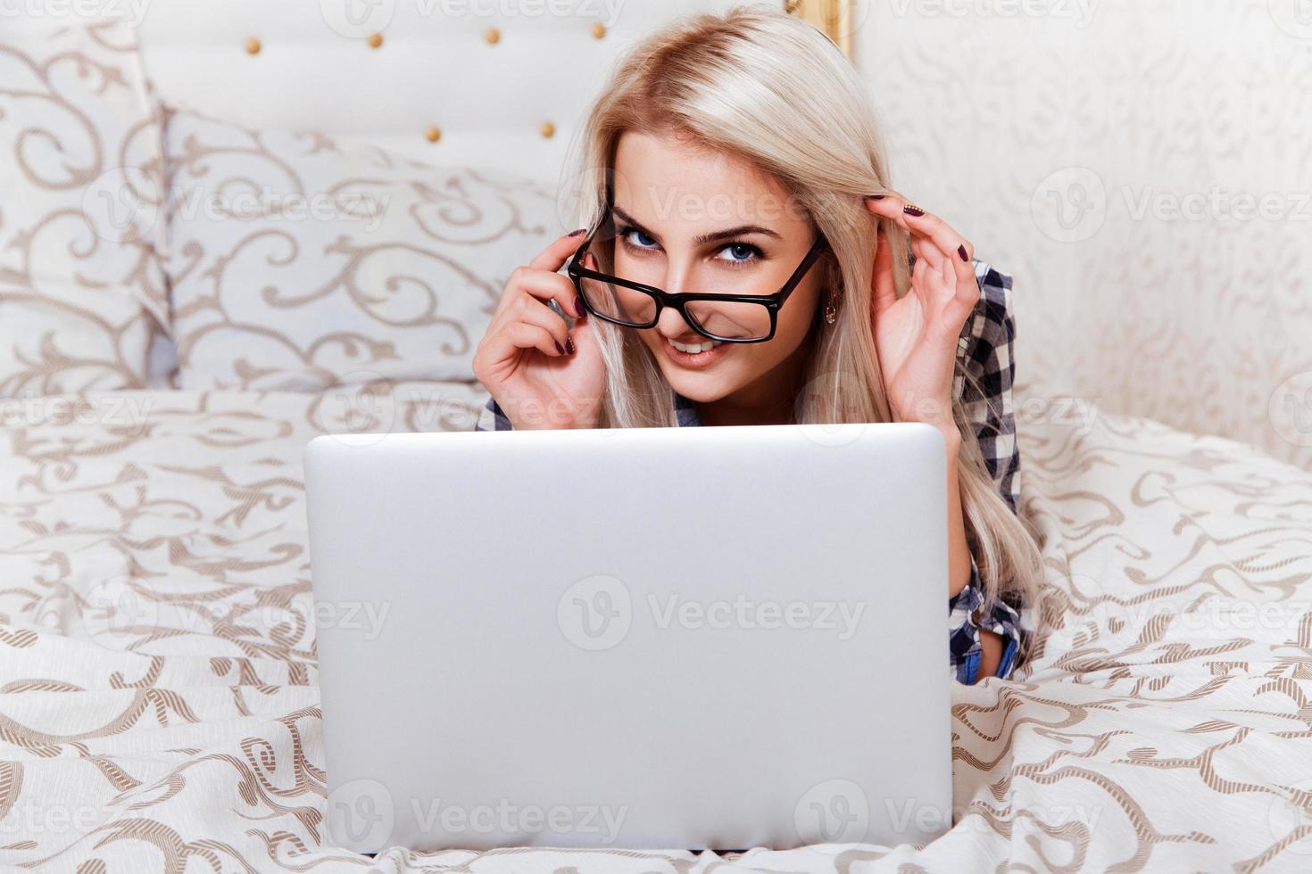 Beauty young blonde woman with blue eyes and laptop smiling on camera in bed photo