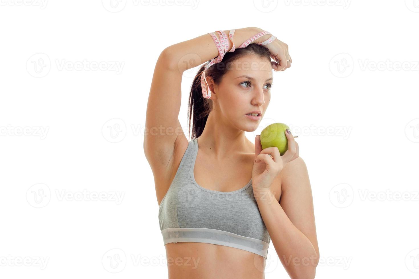 la joven chica de fitness con la parte superior gris levantó la mano y mantiene el primer plano de la manzana verde foto