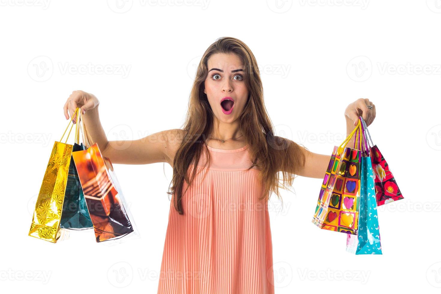 Una joven con gran sorpresa sostiene los regalos de bolsas brillantes de los lados y está aislada de fondo blanco foto