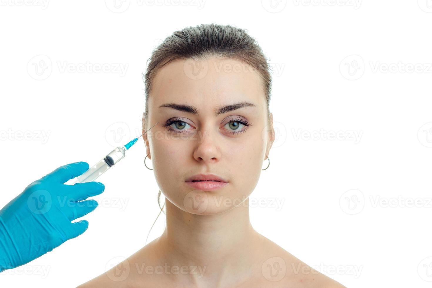 cosmetologist makes injection syringe on the face of a young beautiful girl who looks straight close-up photo