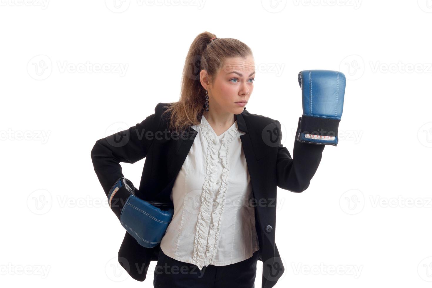 joven y hermosa rubia con guantes de boxeo y chaqueta con camisa se para en el estudio y levanta la mano foto