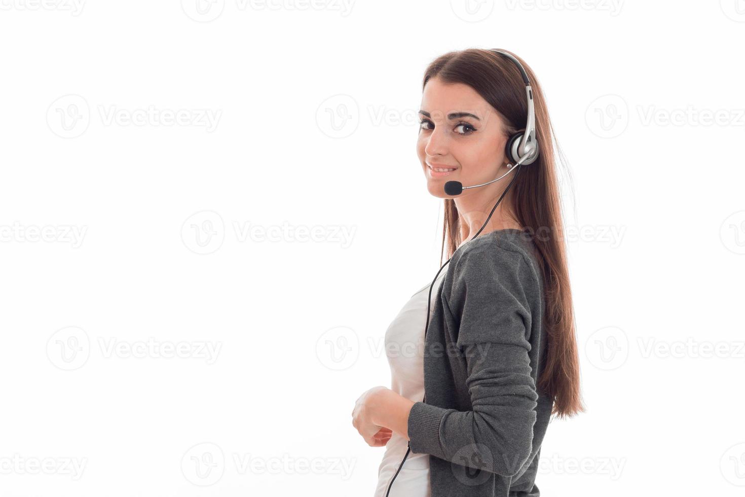 smiling young woman in a gray jacket and headphones stands sideways and looking at camera photo