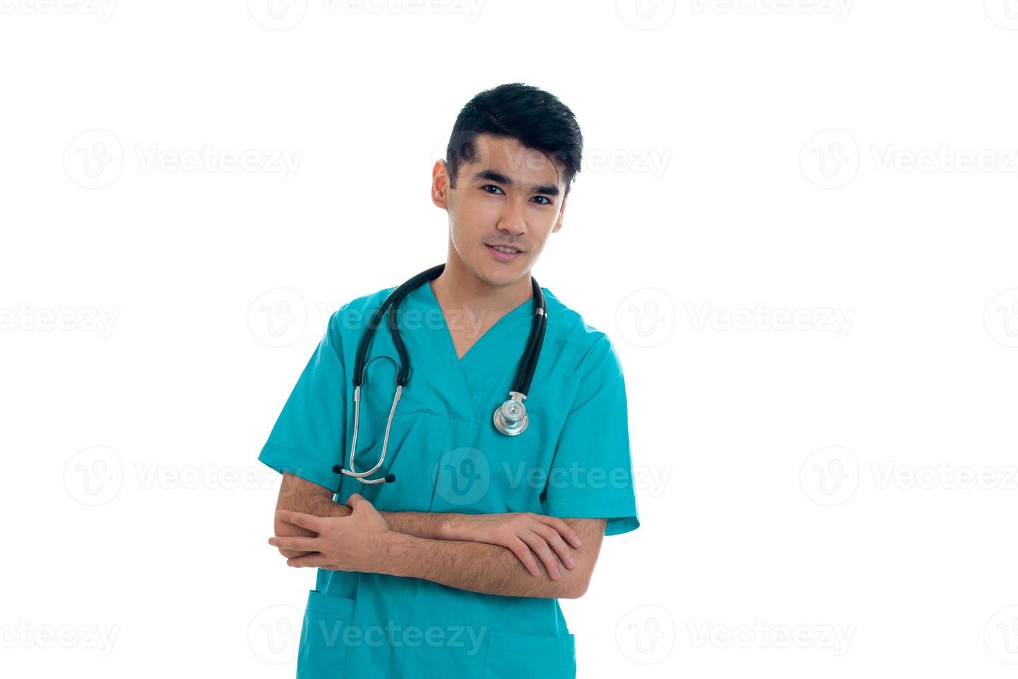bastante elegante doctor en uniforme azul con estetoscopio posando y sonriendo en cámara aislada sobre fondo blanco foto