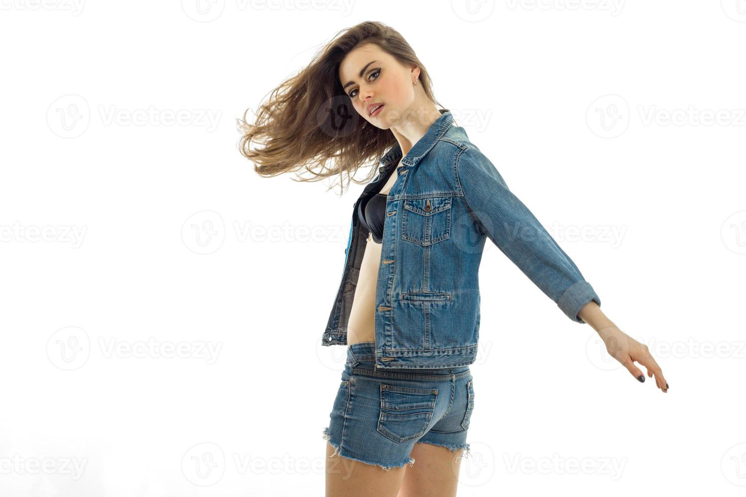 great young brunette with beautiful developing hair in a jeans suit, keeping her hand in the face and looks at the camera photo