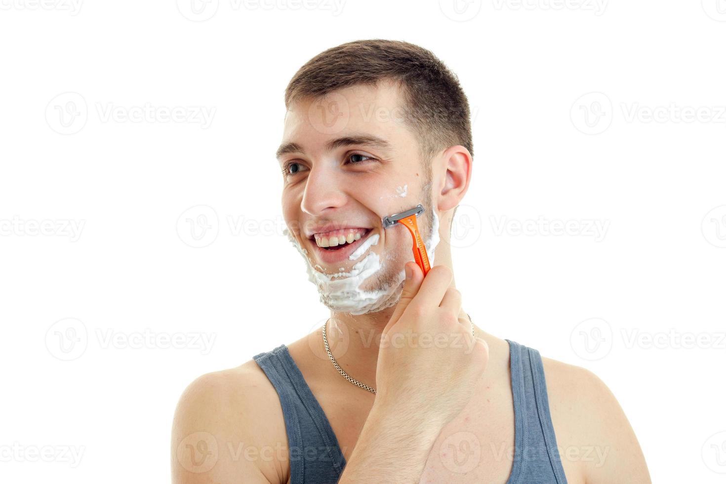 Portrait of a beautiful, cheerful guy who turned his head toward laughs and shaves his beard with foam on his face photo