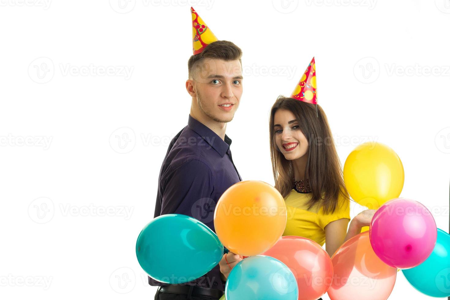 alegre pareja joven celebra cumpleaños con grandes globos y conos en la cabeza y sonriendo foto