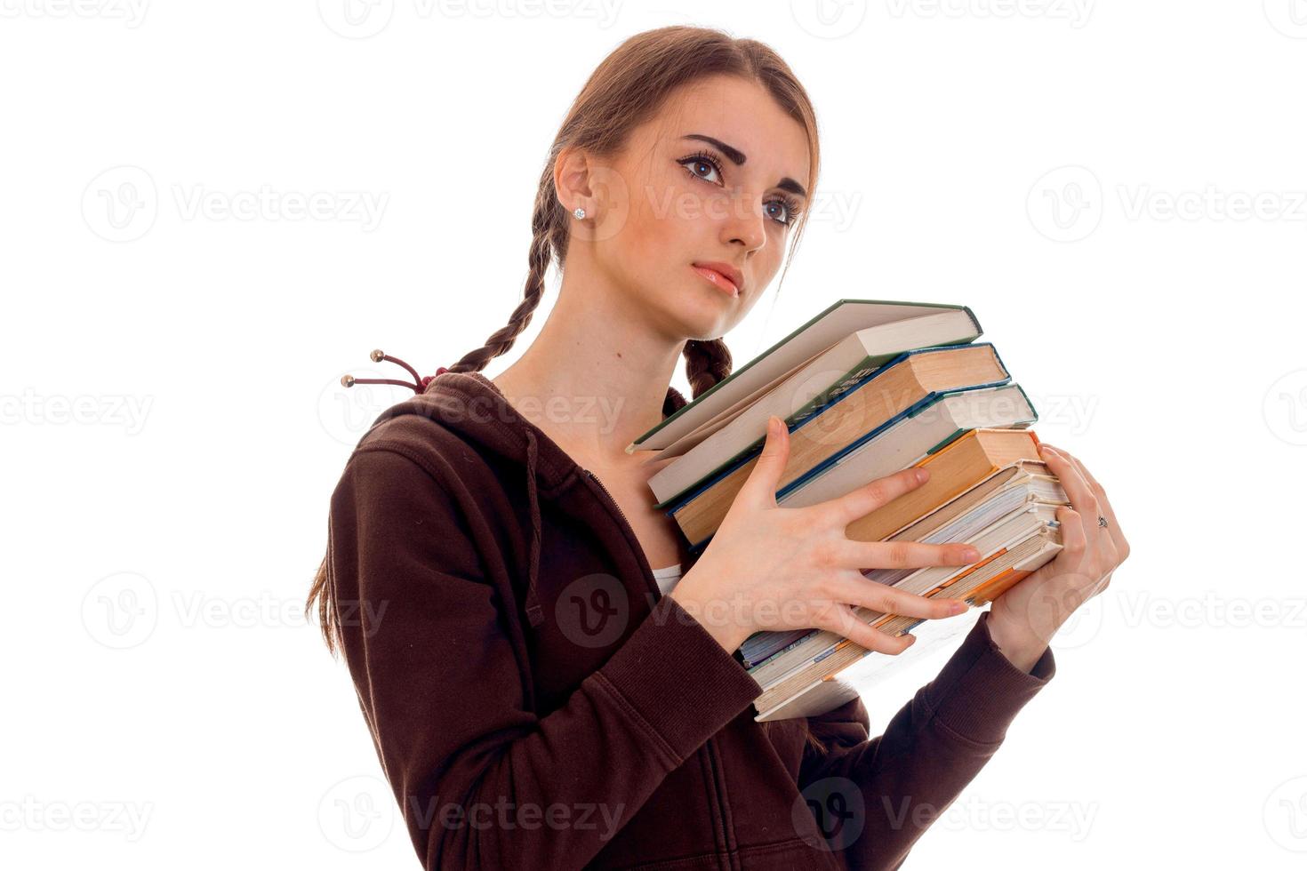 tired young brunette student girl in brown sport clothes with a lot of books in her hands posing isolated on white background photo