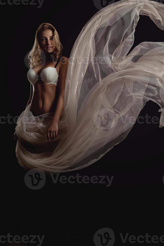 Vertical photo of sexual blonde woman in white bra and flying fabric