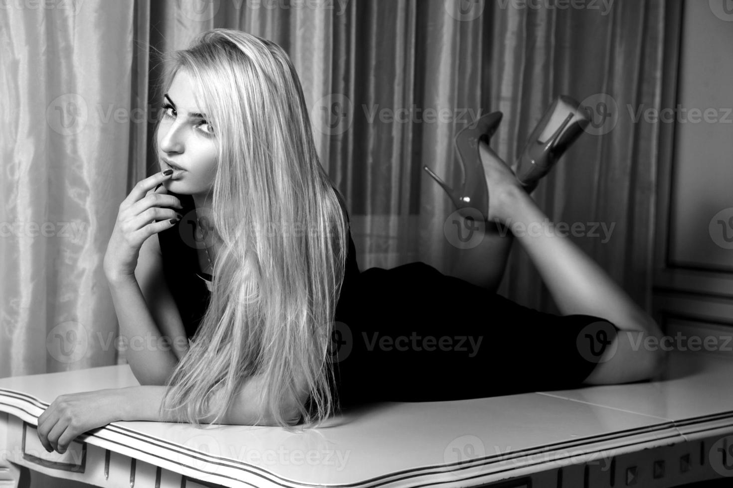 Black and white portrait of charming blonde woman with seduction look on table photo