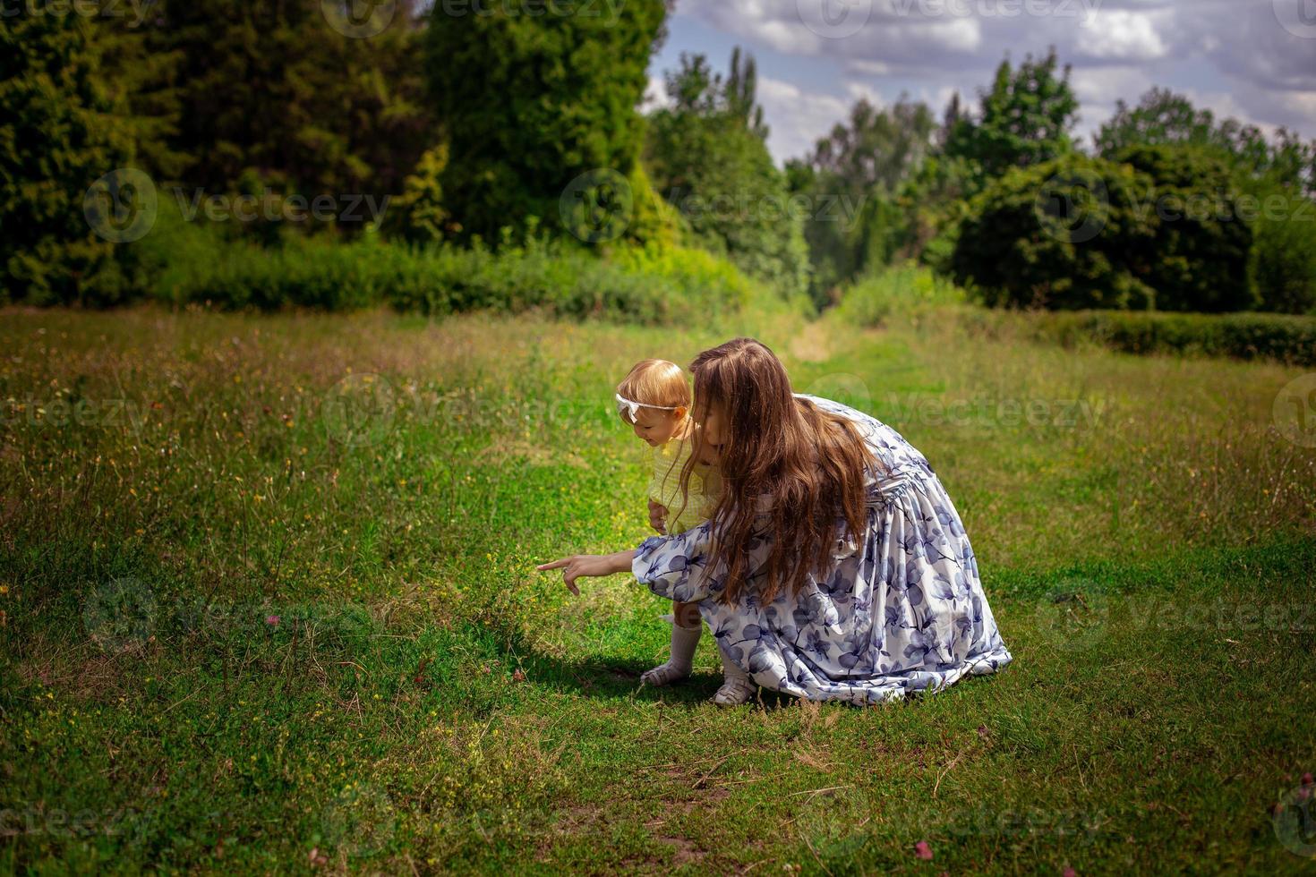 Mom points finger her little daughter to the green grass at the garden photo