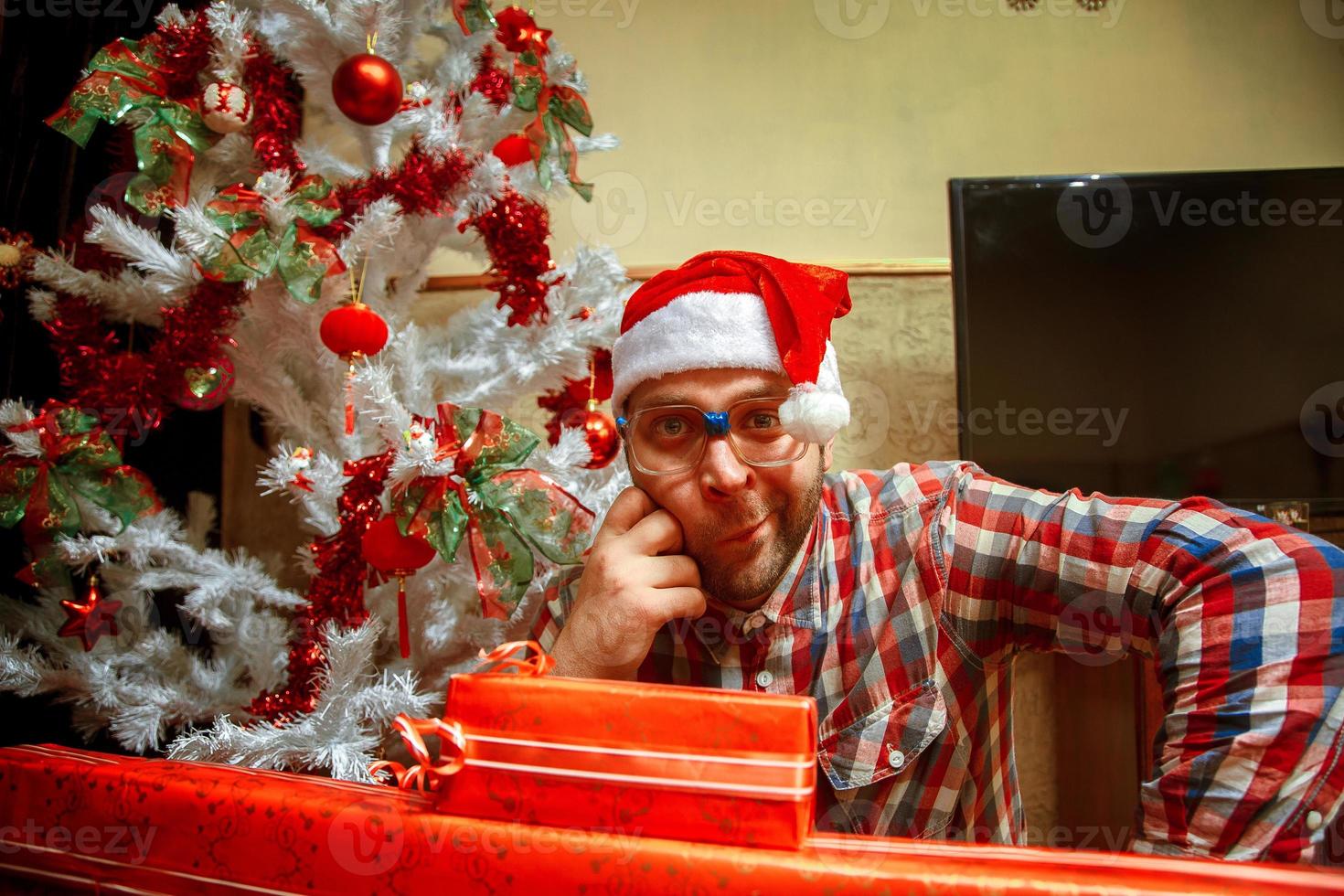 Fun nerd in glasses and santa hat near christmas tree photo
