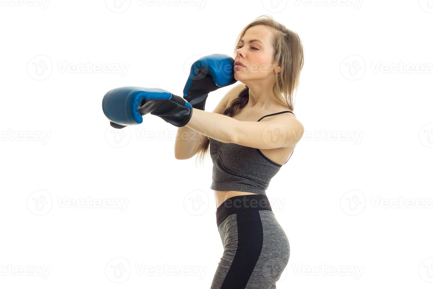 Slim young blonde stands sideways and boxes in gloves close-up photo