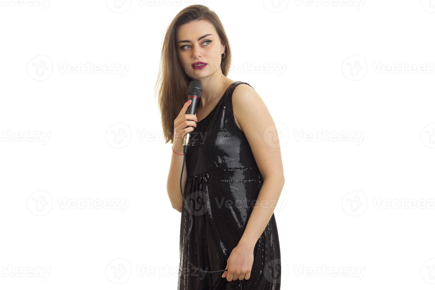 Chic young women in a sleek black dress with a microphone in her hand photo