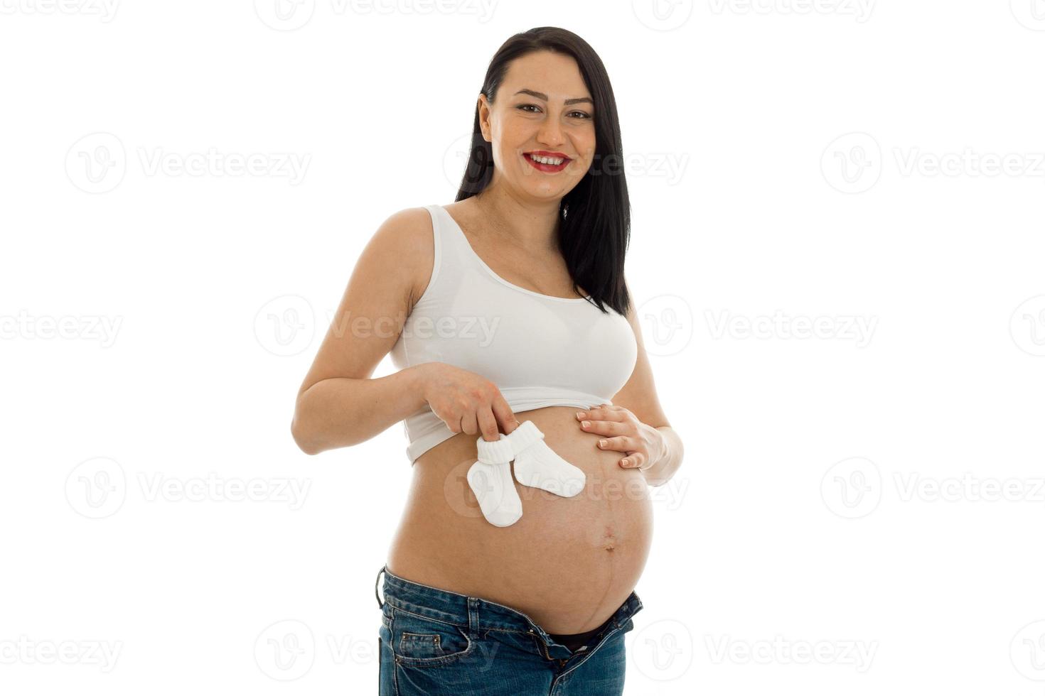studio portrait of young pregnant brunette woman with little socks in her hands smiling on camera isolated on white background photo