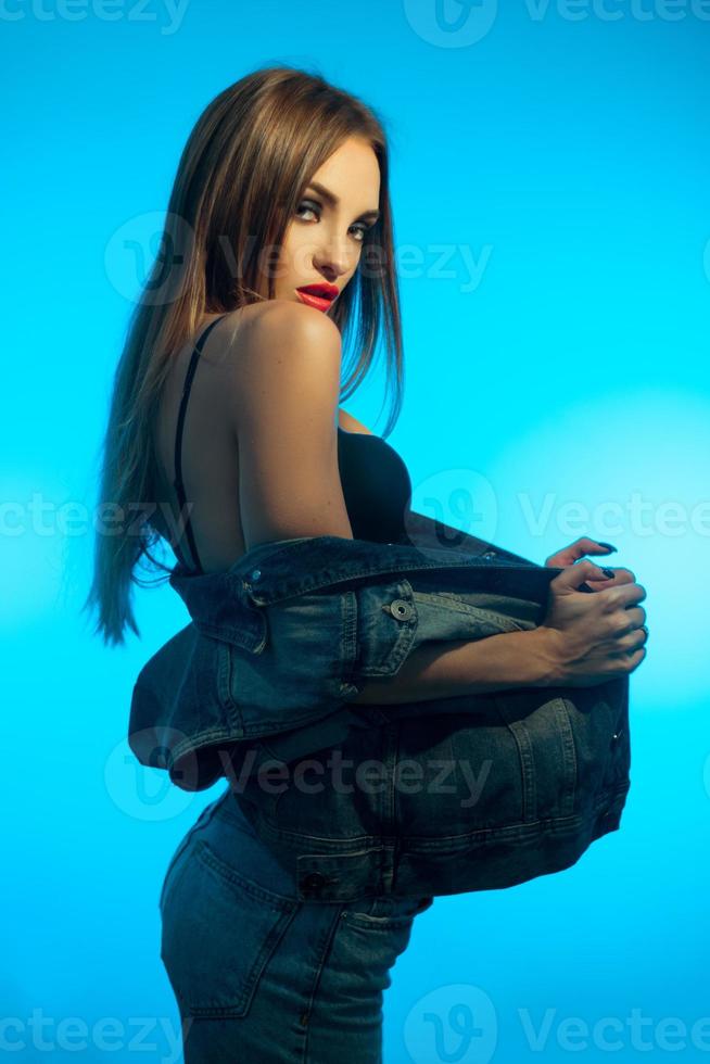 glamour young girl with red lips wearing a jeans clothes and looking at the camera on blue background photo