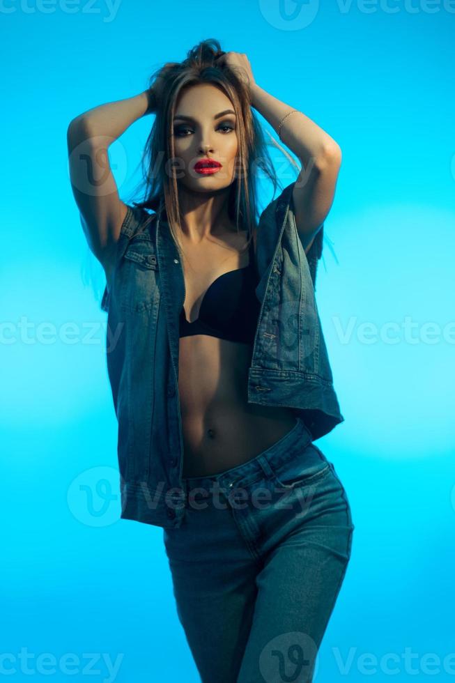 young beautiful girl with red lips in denim clothes posing on camera on blue background photo