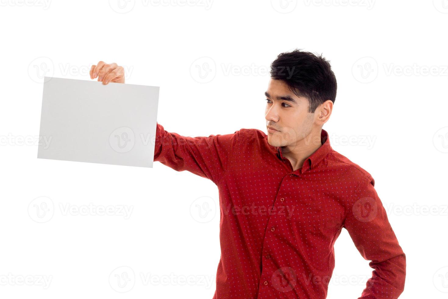 joven moreno con camiseta roja posando con un cartel blanco en la mano aislado en el fondo foto