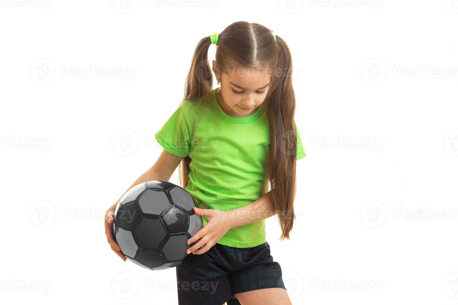 niña rubia con uniforme verde jugando con una pelota de fútbol foto