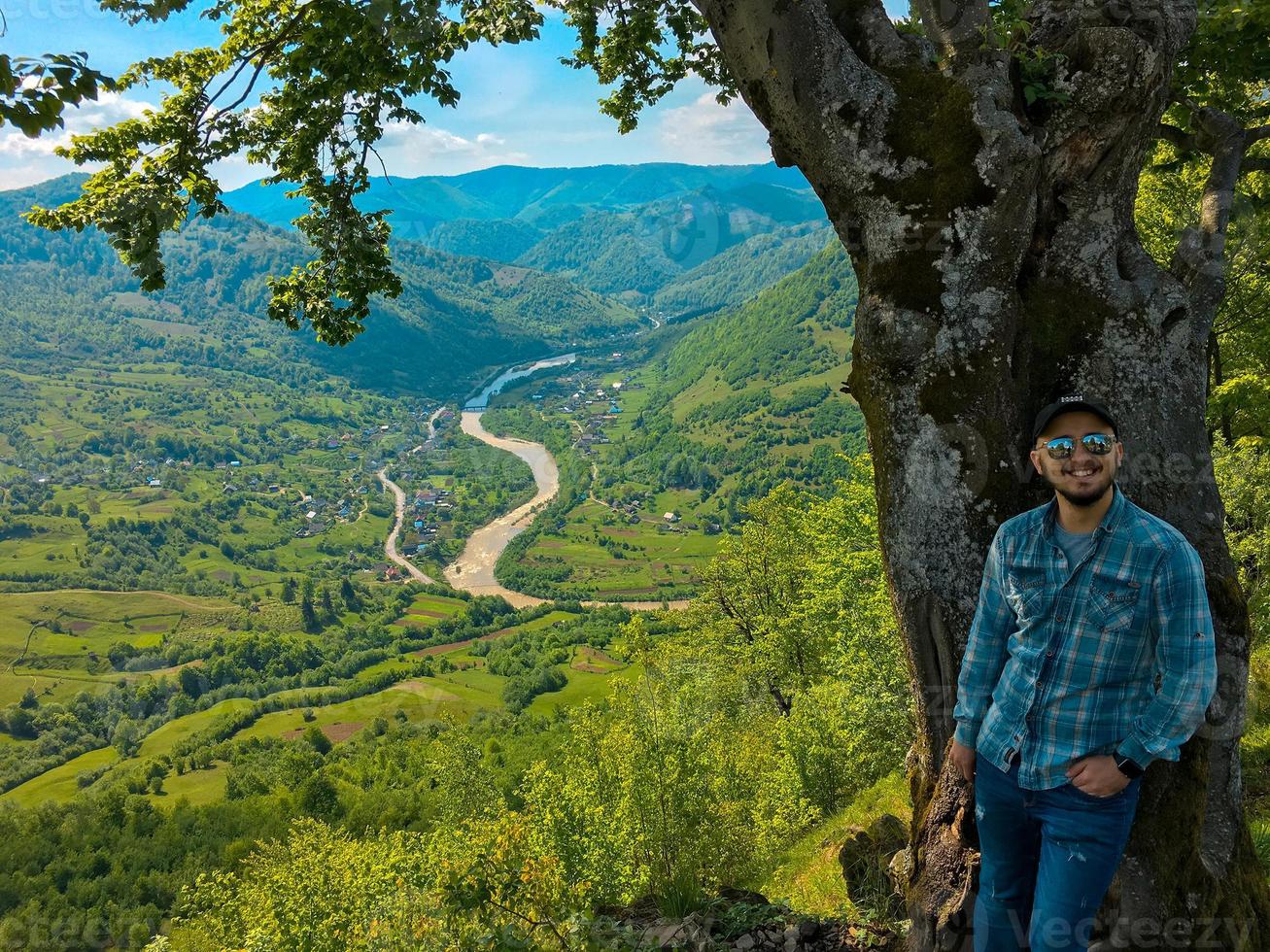 guy posing near tree with view on mountains and river photo