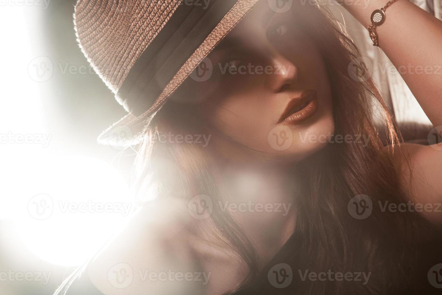 Stylish young adult woman in hat looking at camera. Studio shot photo