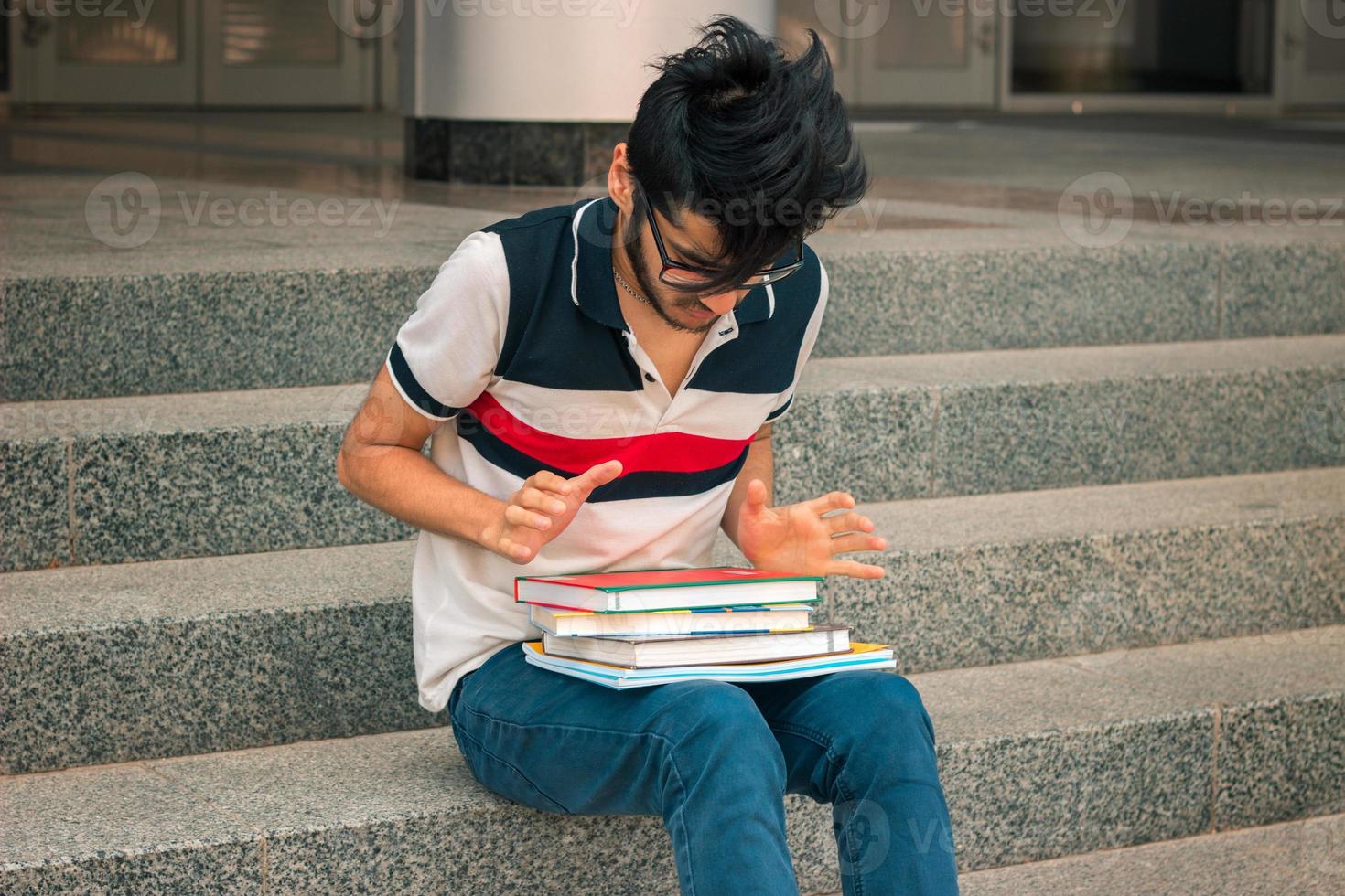 young student sits on the steps and looks at books photo
