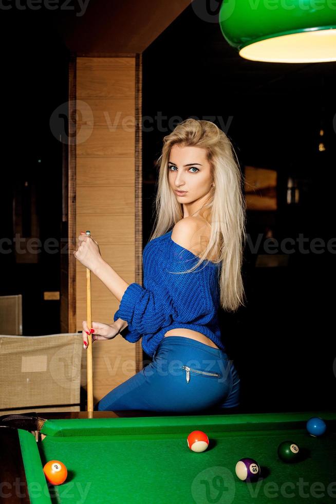 Hot young blonde woman posing on the pool table with the cue photo
