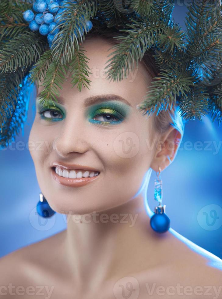 Charming young woman smiling in studio with xmas tree-wreath on head photo