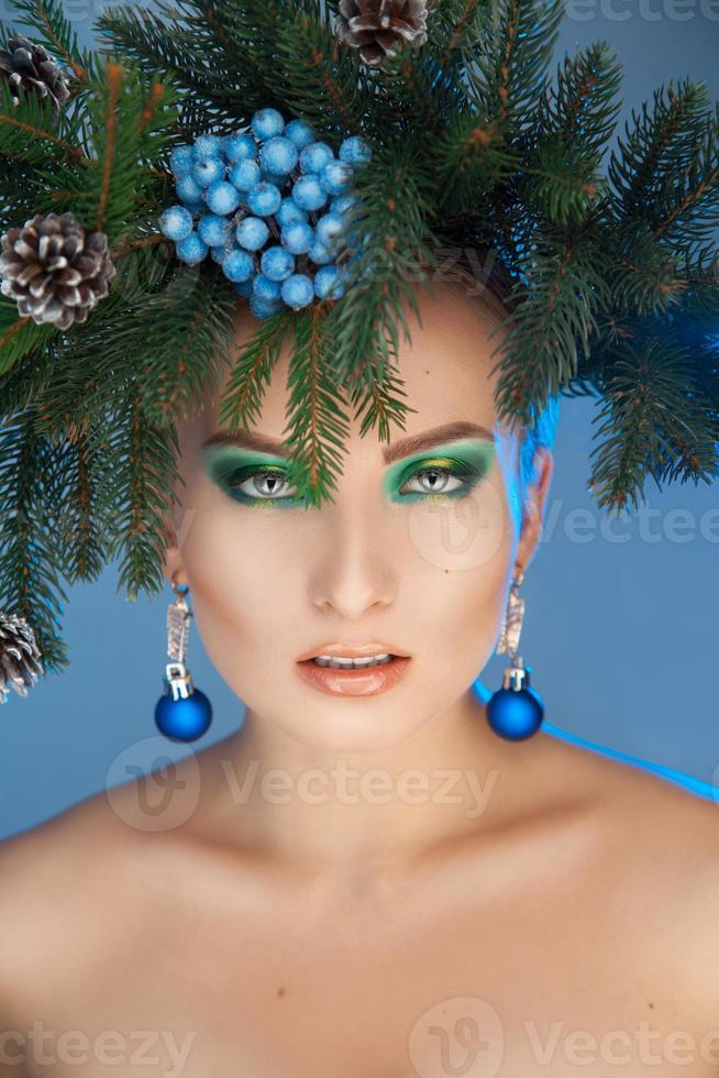 Serious young woman with nice makeup and xmas tree-wreath on head looking at camera photo