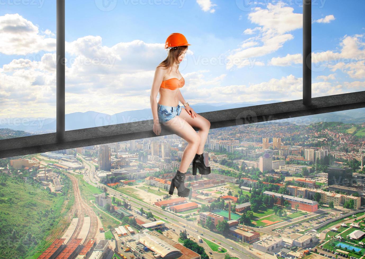 woman builder in helmet sits on a crossbar photo