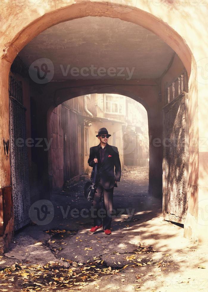 man in a suit and hat and red shoes goes through the arch photo