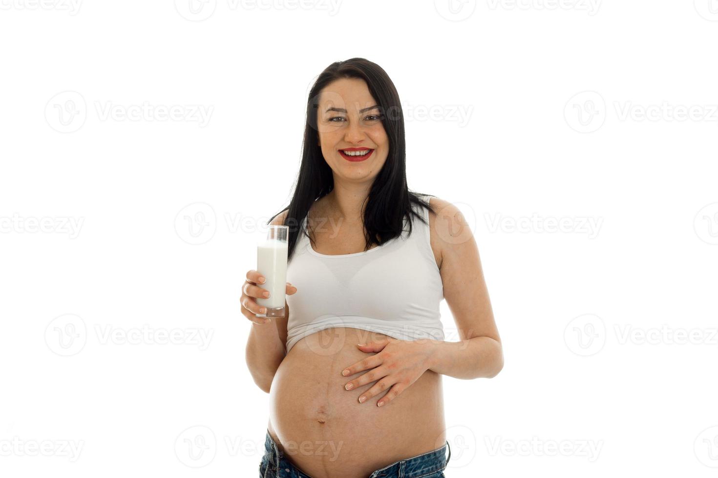 Young cheerful pregnant mother isolated on white background in studio laughing and posing with glass of milk photo