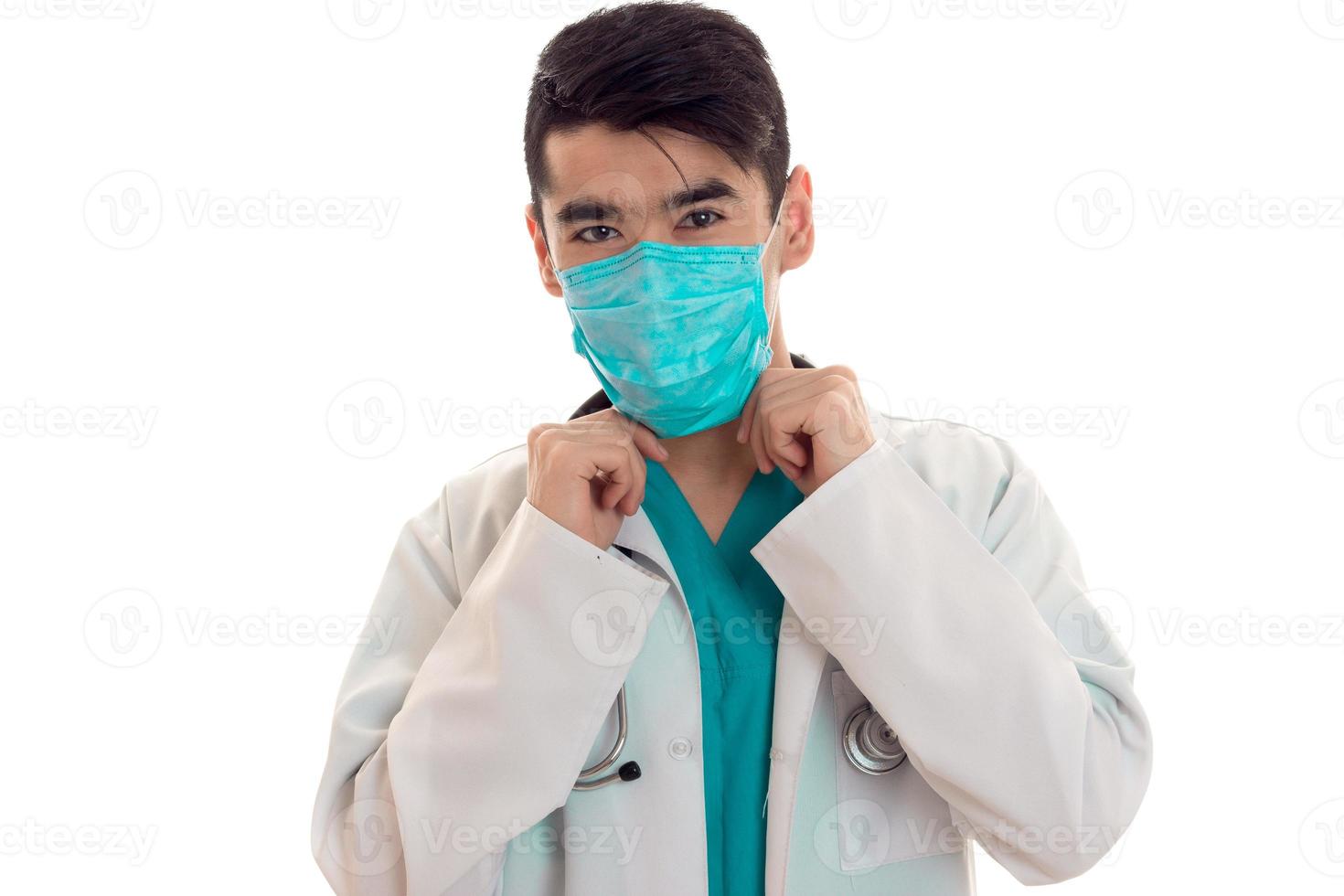 young handsome man doctor posing in uniform and mask isolated on white background in studio photo