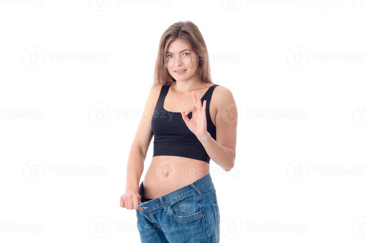 Slim young girl in black top stands in the large size trousers isolated on white background photo