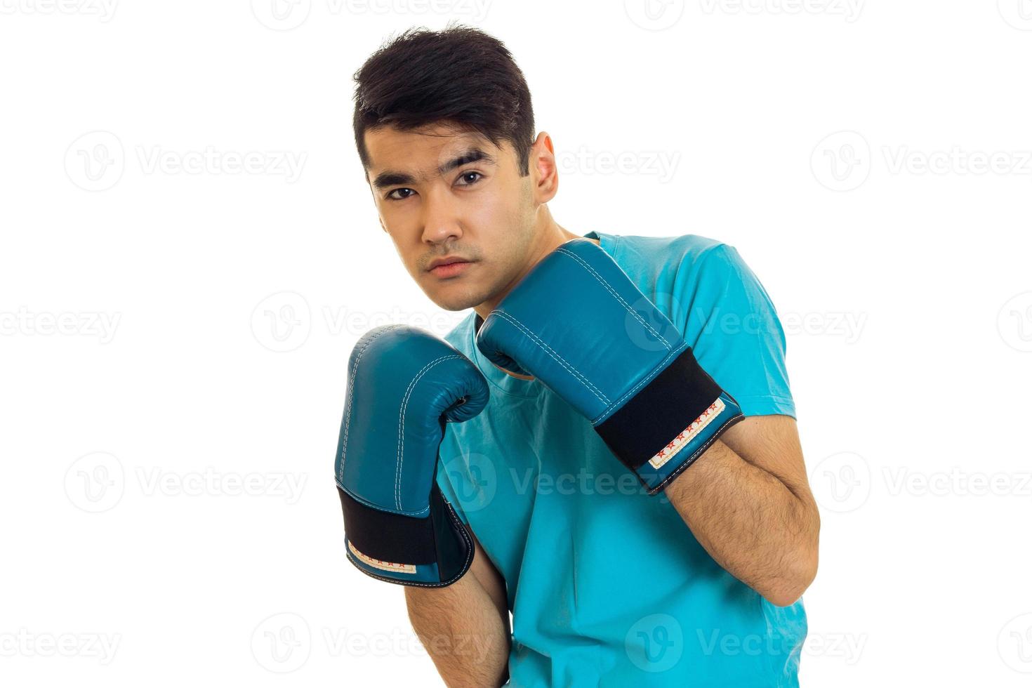 handsome brunette sportsman in blue boxing gloves and uniform practicing boxing isolated on white background photo