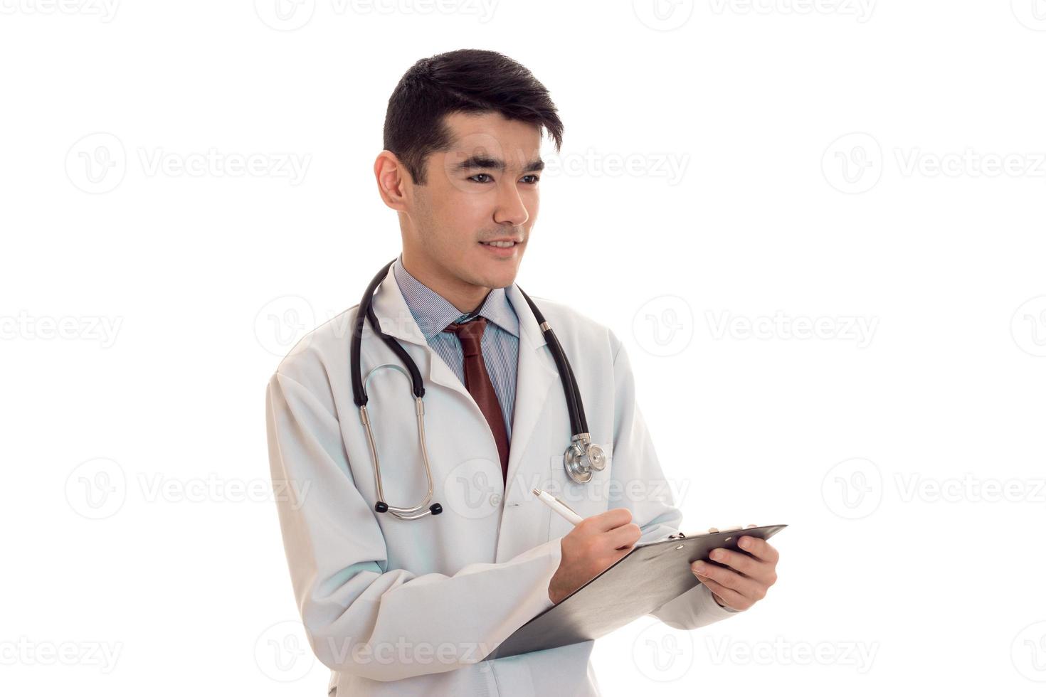 Bonito médico masculino en uniforme con estetoscopio hace notas aisladas sobre fondo blanco. foto