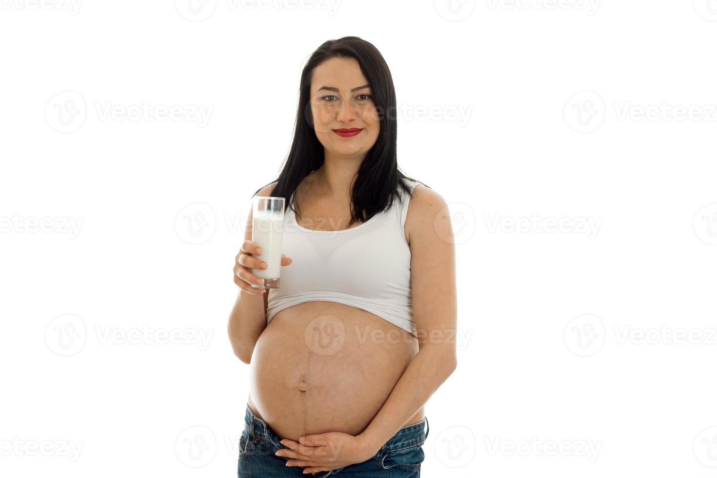 pretty young pregnant brunette woman touching her belly and drinks milks isolated on white background photo