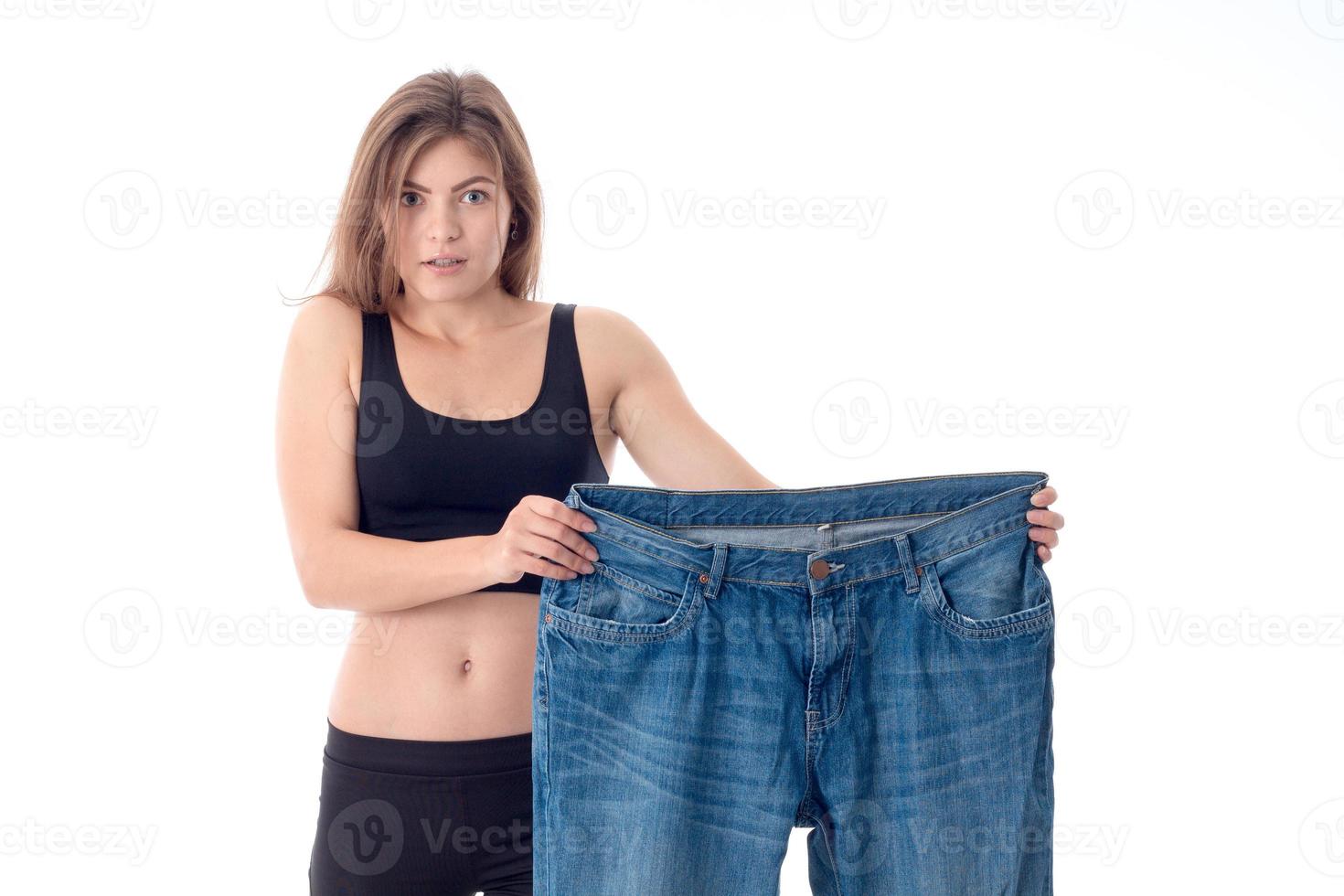 girl in black sportswear holds huge pants isolated on white background photo