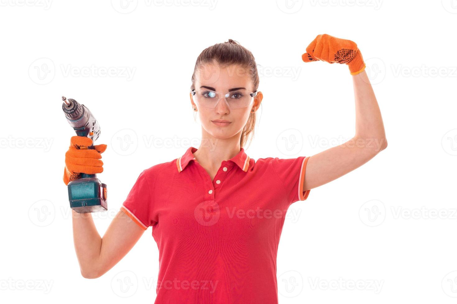 beauty young brunette builder girl in uniform and glasses makes renovation with drill in hands isolated on white background photo